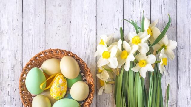 Eggs in a basket and flowers on a padded wooden background
