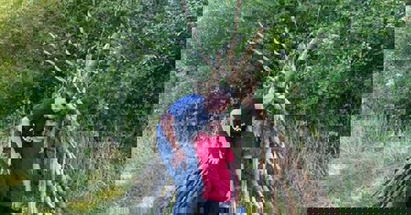 Two children stood in front of a den made of tree branches