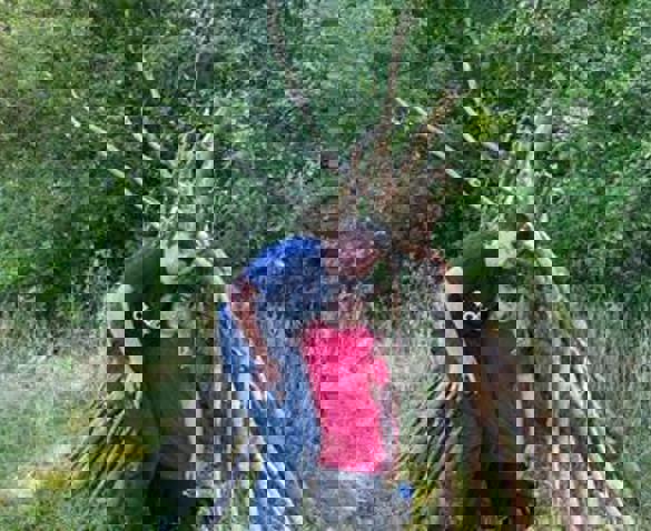 Two children stood in front of a den made of tree branches